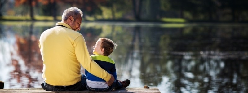 Father and son sitting by water and smiling